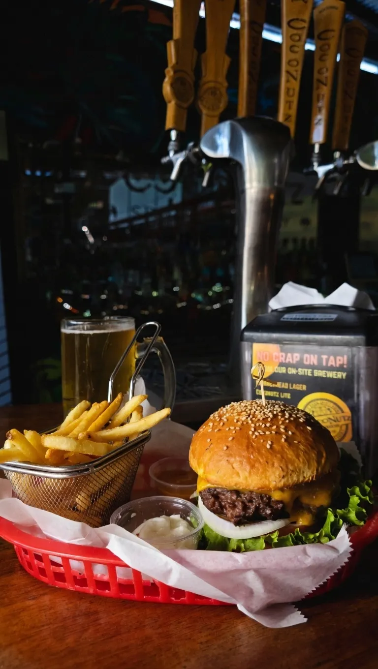 Una deliciosa hamburguesa con papas fritas y cerveza Coconutz en la mesa